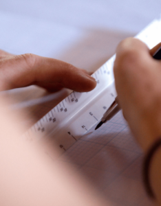 A UGA CED student uses a pen and ruler on graph paper.