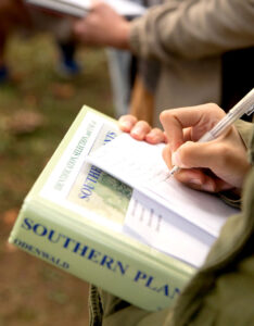 Student taking notes while holding a Southern Plants field guide.