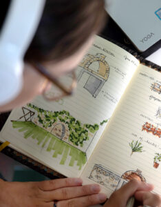 MLA student sketching outdoor kitchen designs in a notebook.