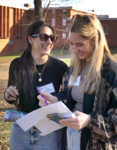 Two students smiling while writing notes outdoors.