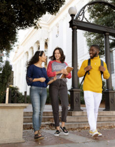 Three UGA students walk and talk near the university’s historic Arch on campus.
