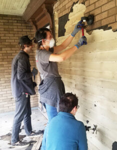 Students remove siding from a historic house wall as part of a hands-on preservation project.
