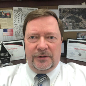 Portrait of Charlie Gluodenis, Chief Real Estate Officer for the Athens Housing Authority, wearing a white shirt and tie in an office setting.