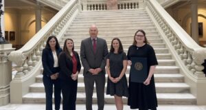A group of five people standing in front of stairway at the Georgia State Capitol. Mayo, far right, holds an award.