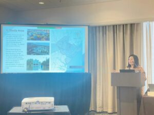 Jiyue Zhao presents powerpoint slides on sea level rise in Chatham County, GA from a podium.